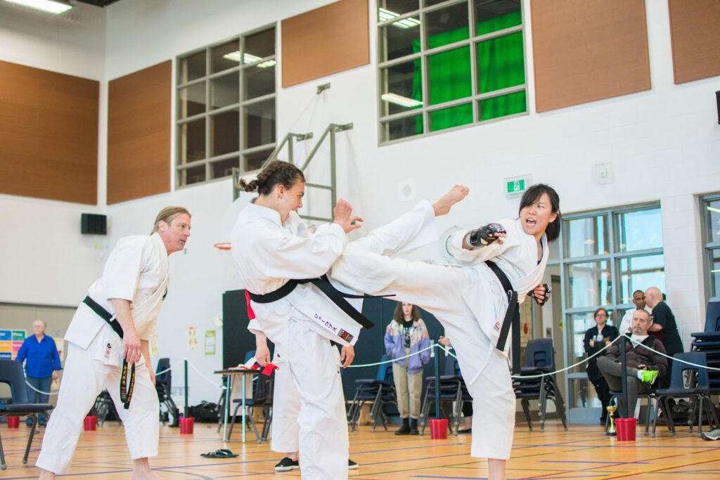 two female black belts kick each other in a sparring match